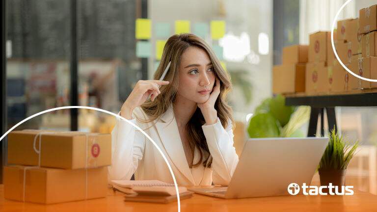 Imagem mostra jovem mulher com notebook à frente e caixas atrás dela, com feição de dúvida, como se perguntasse se MEI pode vender na Amazon