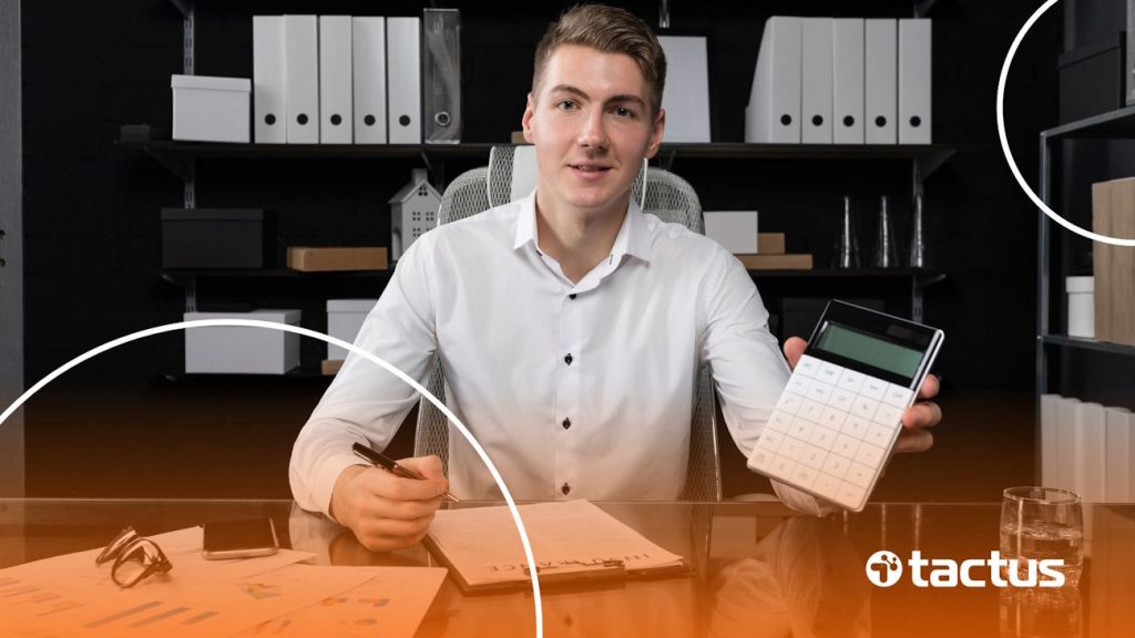 Imagem mostra jovem de negócios em sua mesa com calculadora na mão olhando para a câmera, para simular o que muda com a reforma tributária para representantes comerciais