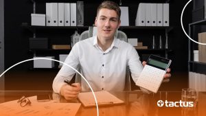 Imagem mostra jovem de negócios em sua mesa com calculadora na mão olhando para a câmera, para simular o que muda com a reforma tributária para representantes comerciais