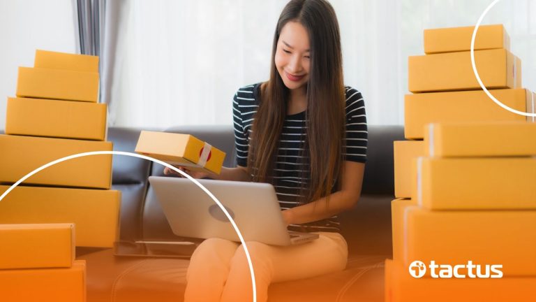 Imagem mostra mulher sorridente mexendo no notebook e cercada por caixas, para simbolizar como ser ponto de coleta do Mercado Livre