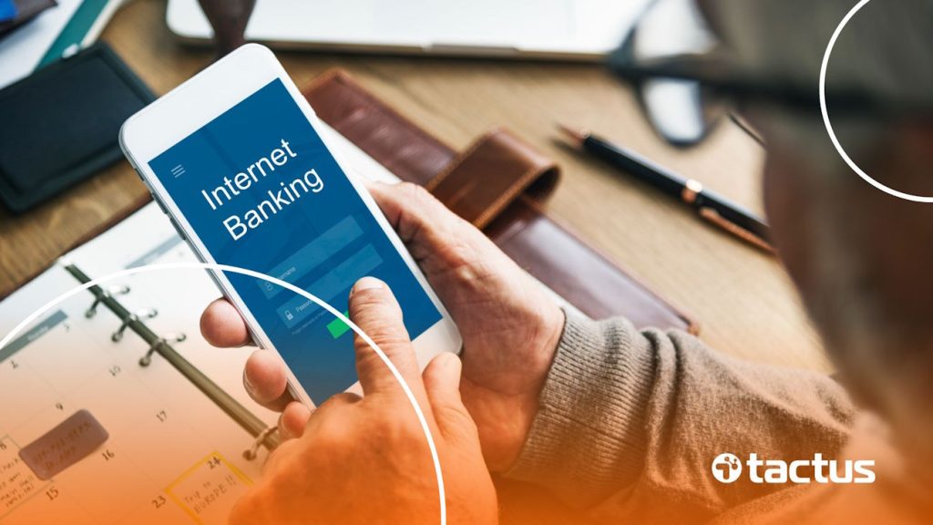 Imagem mostra empresário mexendo no celular com a tela escrita "Internet Banking", para ilustrar a forma correta de transferir dinheiro da empresa para conta pessoal