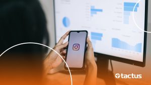 Imagem mostra mãos de jovem mexendo no Instagram, com tela à frente de computador repleta de gráficos, para simbolizar como monetizar o Instagram