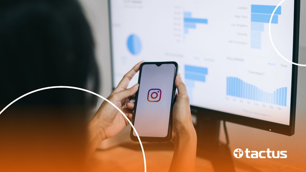 Imagem mostra mãos de jovem mexendo no Instagram, com tela à frente de computador repleta de gráficos, para simbolizar como monetizar o Instagram