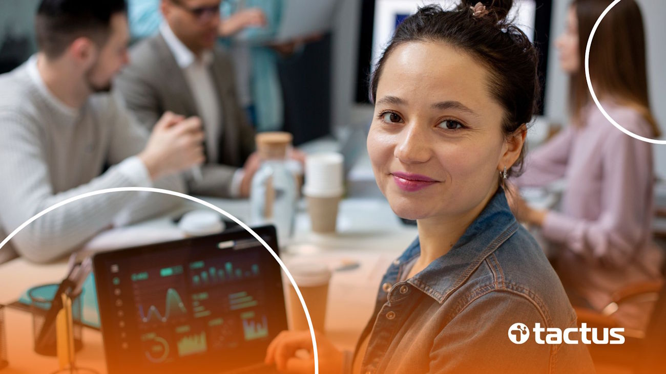Imagem mostra jovem mulher com notebook com gráficos e mesa com outros executivos em segundo plano, para ilustrar o trabalho de um gestor de automação