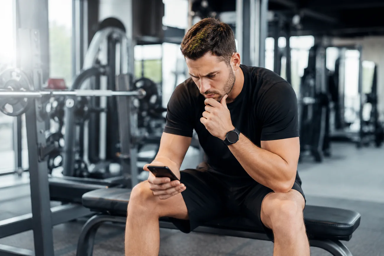 Imagem mostra personal trainer olhando para o celular e pensando se personal trainer pode ser MEI