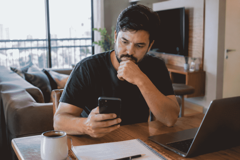 Imagem mostra profissional autônomo em casa olhando para o celular com expressão de preocupação, querendo saber como vai funcionar o CNPJ para pessoa física