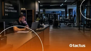 Dono de academia pensativo diante do notebook na recepção, com a academia vazia ao fundo, refletindo sobre os impactos da reforma tributária para academias