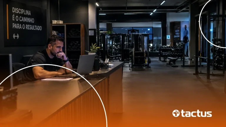Dono de academia pensativo diante do notebook na recepção, com a academia vazia ao fundo, refletindo sobre os impactos da reforma tributária para academias